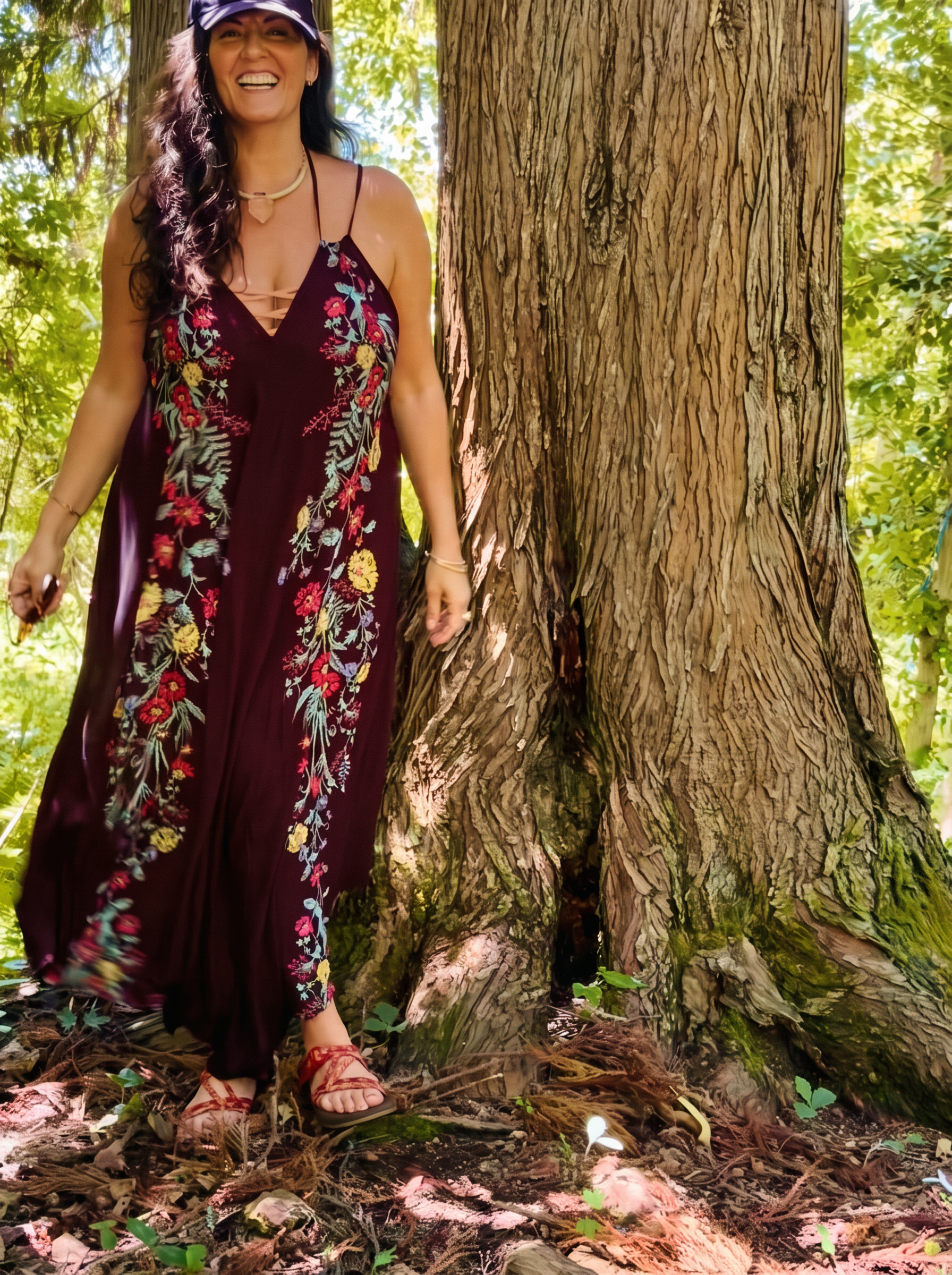 Bettie in a floral dress laughing beside an ancient cedar tree in the forest